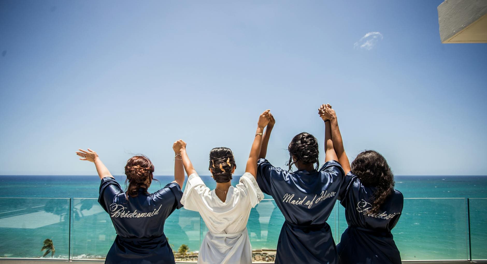 four women holding hands while facing body of water